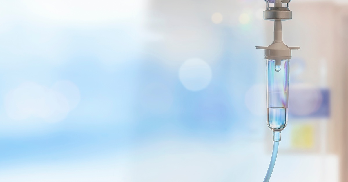 A close-up view shows a clear plastic tube with an IV bag on top. Liquid is dripping into the tube from the bag.