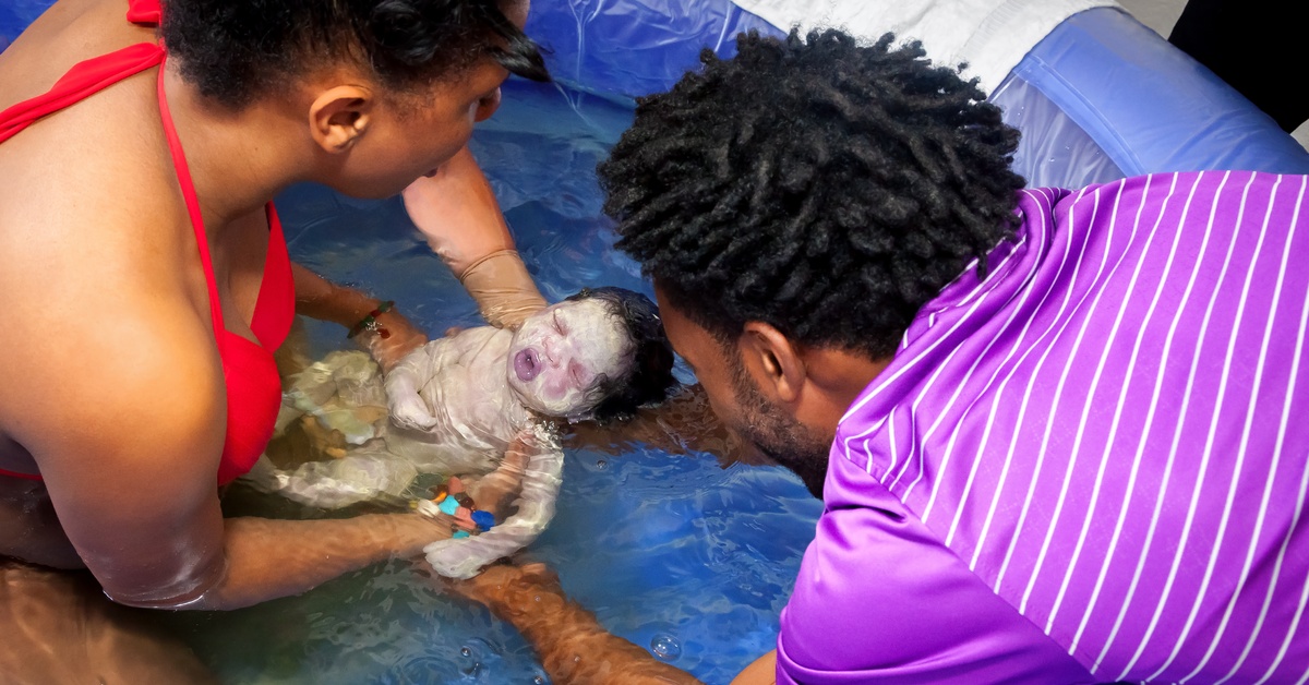 What To Do With Birthing Supplies After a Home Birth A close-up view shows a mother holding a newborn in a blue birthing pool. The father leans over the side of the pool.