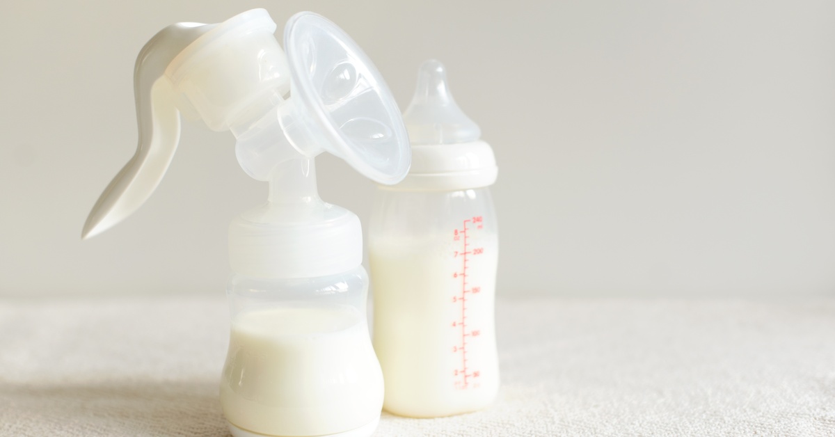 A manual breast pump attached to a plastic bottle filled with milk sits next to a small plastic baby bottle filled with milk.