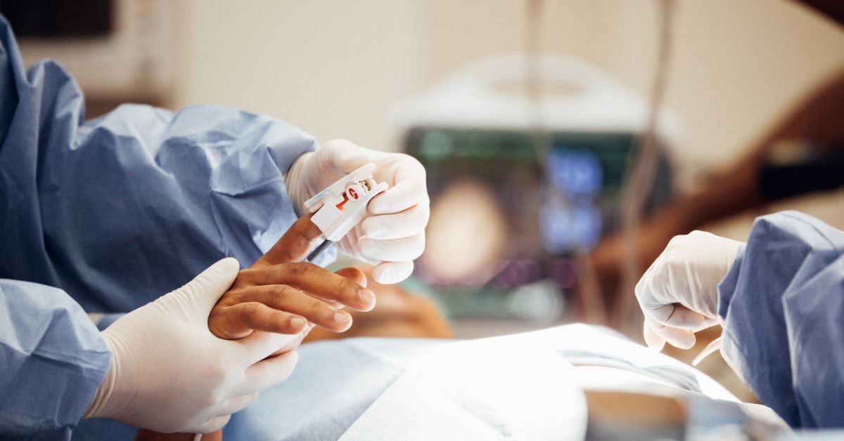 A healthcare professional is applying a white pulse oximeter to the pointer finger of a patient in a hospital setting.