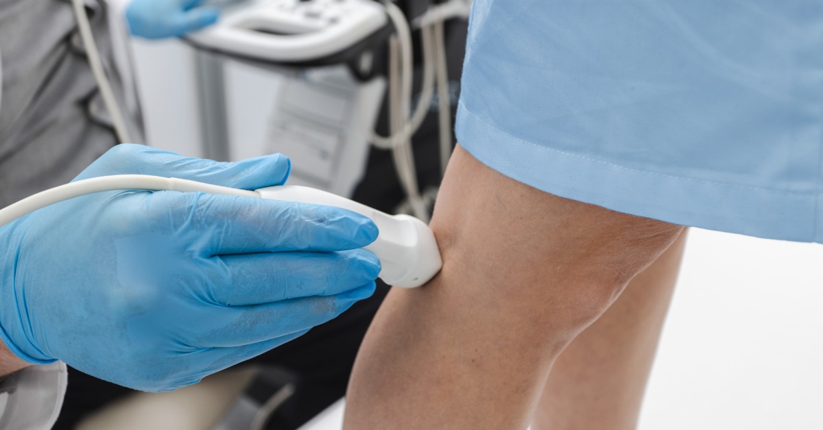 A close-up view shows a medical professional wearing a blue latex glove holding a Doppler probe up to a patient's leg.