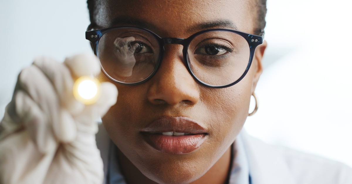 A close-up view shows a female healthcare professional wearing glasses and white latex gloves holding a penlight.