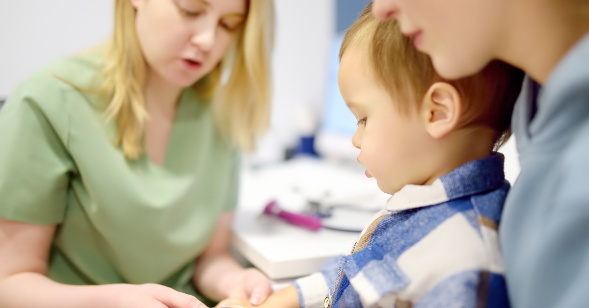 A young boy sits on his mother's lap as a medical professional places a pulse oximeter on his index finger.