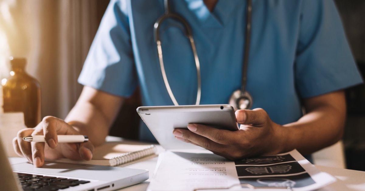 Reading Product Specs When Buying Medical Supplies Online A close-up view shows a medical professional holding a tablet in one hand and touching a laptop touchpad with the other.