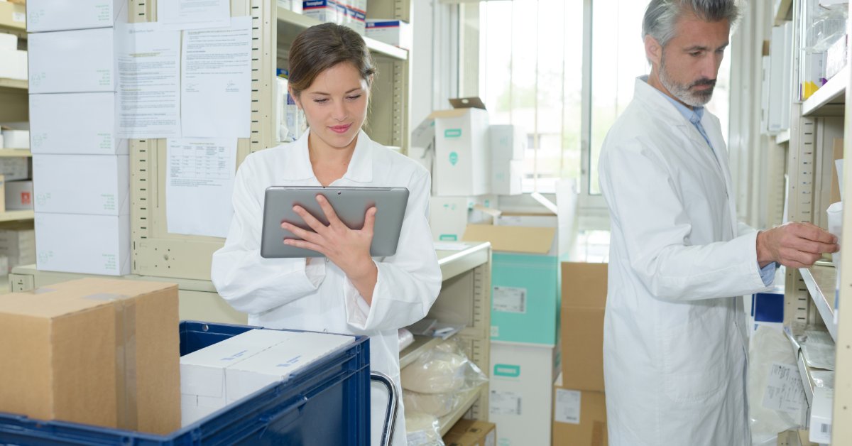 A female medical professional is looking at a tablet, while a male medical professional observes medical products.