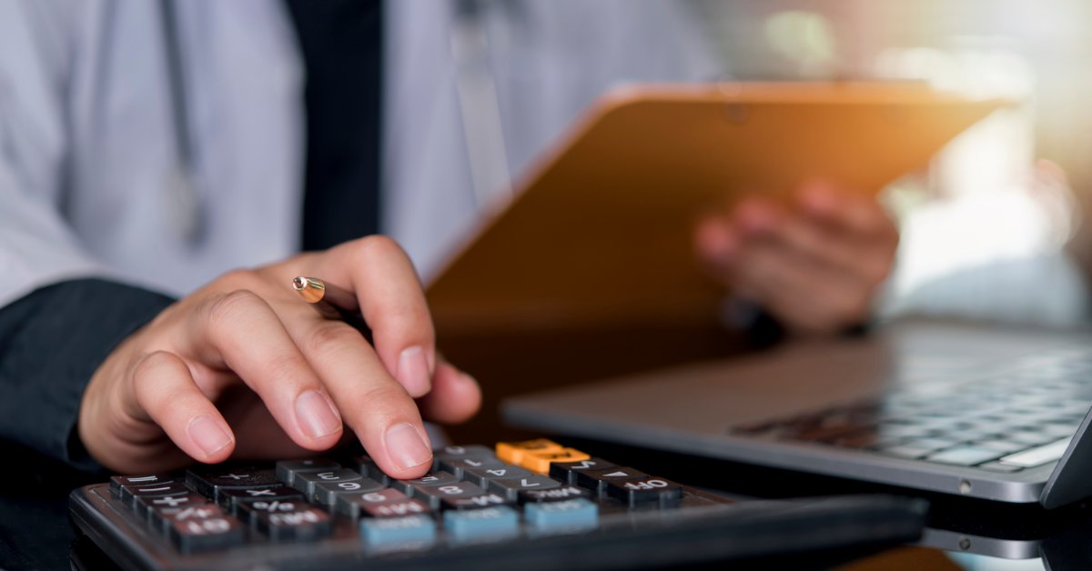 A close-up view shows a person pressing the buttons on a small calculator with a pen between their fingers.