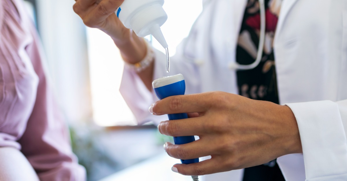 A close-up view shows a healthcare professional squeezing a clear gel onto a Doppler in front of a pregnant patient.