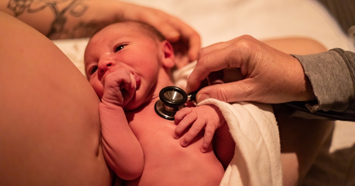 A midwife uses a stethoscope to check a newborn’s heartbeat while the baby rests on a parent’s chest after birth. A midwife uses a stethoscope to check a newborn’s heartbeat while the baby rests on a parent’s chest after birth.