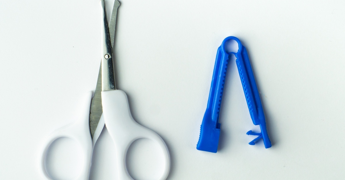 A pair of scissors and a blue umbilical cord clamp, set against a white background, are essential tools for newborn delivery.
