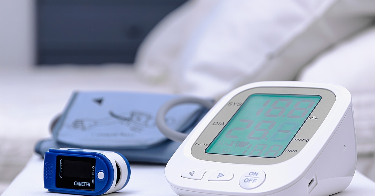 An electronic blood pressure monitor, pulse oximeter, and a blood pressure cuff are on a white table in a medical setting. An electronic blood pressure monitor, pulse oximeter, and a blood pressure cuff are on a white table in a medical setting.