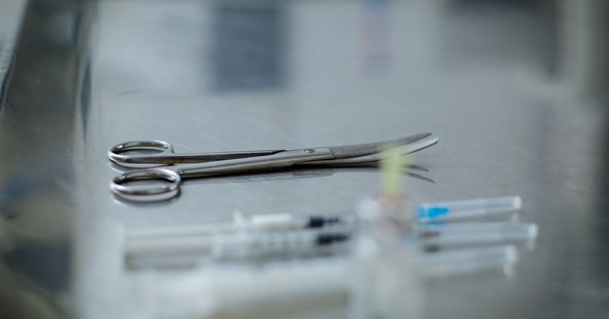5 Medical Instruments Used During IUD Procedures Curved stainless steel surgical scissors are on an operating table, alongside medical syringes, in a surgical room.
